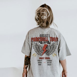 May include: A gray t-shirt with a graphic print of a lightning bolt with wings and the text "Megan's Farewell Tour May 2024". The shirt also has the text "Guest Stars" and a list of names.