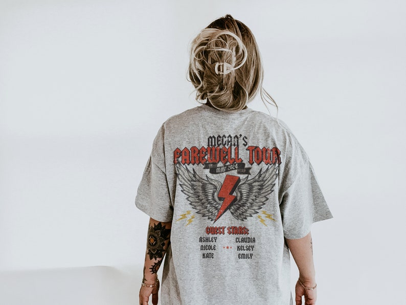 May include: A gray t-shirt with a graphic print of a lightning bolt with wings and the text "Megan's Farewell Tour May 2024". The shirt also has the text "Guest Stars" and a list of names.