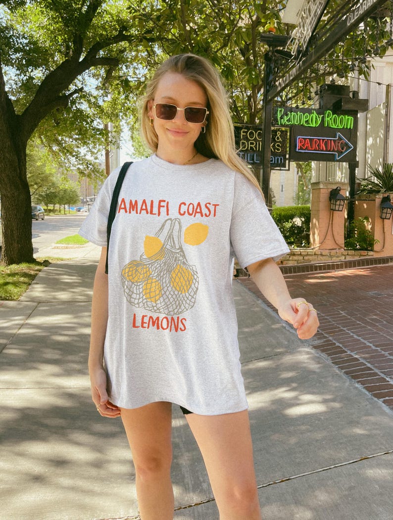 May include: A grey t-shirt with a graphic of lemons in a mesh bag. The text "Amalfi Coast" and "Lemons" is printed on the shirt.