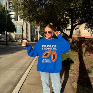 Puede incluir: Una sudadera azul con un gr&aacute;fico de papaya y el texto "Papaya Tropical Rio de Janeiro".