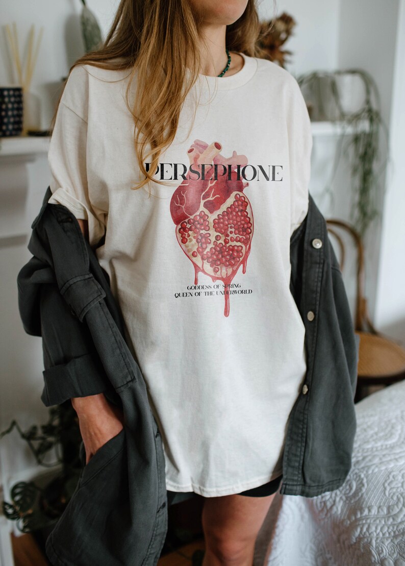 May include: White t-shirt with a graphic of a heart-shaped pomegranate and the text "PERSEPHONE, GODDESS OF SPRING, QUEEN OF THE UNDERWORLD".