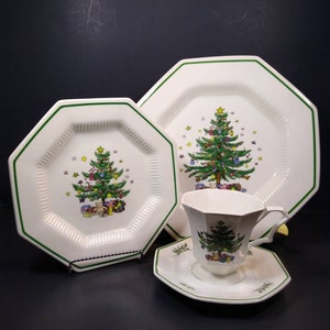 Puede incluir: Juego de vajilla navideña octogonal blanca con ribete verde. El juego incluye un plato, una taza y un platillo, cada uno con un diseño de árbol de Navidad y regalos.
