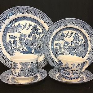 Op de afbeelding: Een set blauw en wit porselein met een wilgenmotief bevat een grote dinerbord, een kleinere saladebord en twee theekopjes met schoteltjes.