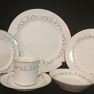 May include: A set of white porcelain dinnerware with a green floral pattern and a gold trim. The set includes a dinner plate, salad plate, soup bowl, cup, and saucer.