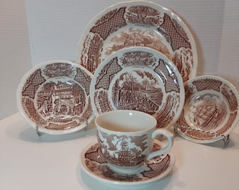 以下が含まれることがあります： 航海をテーマにした、茶色と白の磁器製の食器セット。船や帆走シーンの絵柄が施された茶色と白のデザインです。大きな皿には「Friendship of the Seas」の文字が見えます。