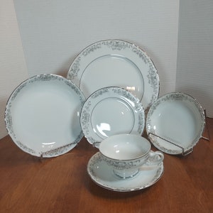 Könnte beinhalten: Ein Set aus weißem Porzellan-Geschirr mit einem silbernen Blumenmuster. Das Set enthält einen großen Speiseteller, einen Salatteller, eine Suppenschüssel, eine Teetasse und eine Untertasse.