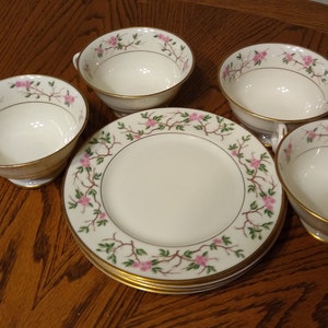 Puede incluir: Juego de cuatro tazas de té blancas y platillos con un diseño floral. Las tazas y los platillos tienen un borde dorado y presentan flores rosas y hojas verdes.