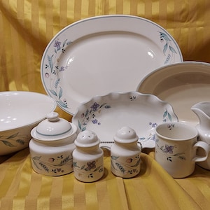 May include: A set of white ceramic dishes with a floral design in shades of blue, green, and pink. The set includes a large oval platter, a smaller oval dish, a round bowl, a creamer, a sugar bowl, and two salt and pepper shakers.
