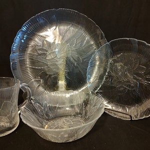May include: A set of four clear glass dishes with a floral pattern. The set includes a large plate, a smaller plate, a bowl, and a mug.