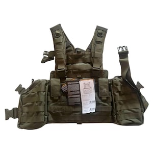 Puede incluir: Chaleco táctico verde oliva con múltiples bolsillos, correas y hebillas. El chaleco tiene correas ajustables para los hombros y cierres laterales. Una etiqueta del producto está adherida al frente. El chaleco está diseñado para transportar equipo.