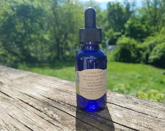 May include: A blue glass bottle with a dropper top and a white label. The label reads "12 Gates Farm", "1225 Bobblett Gap Rd", "Montvale, VA 24121", "540-947-5228", "Violet Extract", "Ingredients: alcohol", "Processed without inspector", "Net Wt. 1 fl oz".