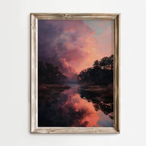 May include: A framed landscape art print depicts a serene scene with a body of water reflecting a vibrant sunset. The sky is filled with shades of pink, orange, and purple, mirrored in the water. Dark silhouettes of trees line the horizon.