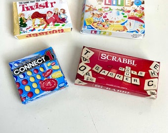 May include: Four miniature board game boxes. The boxes are red, yellow, blue, and white. The games are Scrabble, Connect 4, Life, and Twister.
