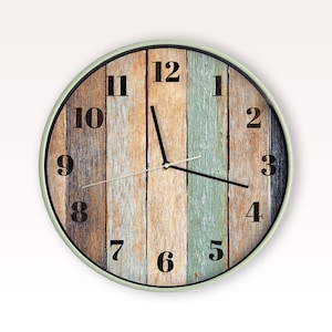 May include: A round wall clock with a light-coloured frame and a face featuring a vertical plank pattern in shades of brown, tan, and muted teal. The clock has black Arabic numerals from one to twelve and thin black hour, minute, and second hands.