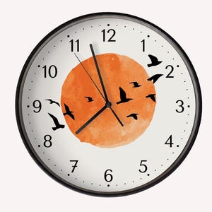 May include: A round wall clock with a black frame and a white face featuring black numerals from 1 to 12. The centre displays a large, textured orange circle with several black silhouettes of birds in flight across the surface. Three black hands.