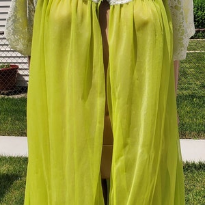May include: A lime green sheer robe with white lace trim and a button closure. The robe is made of a lightweight fabric and has a flowing silhouette.