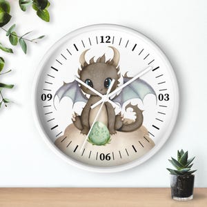 May include: White round clock with black numbers and hands. A cartoon illustration of a brown dragon with purple wings holding a green egg is in the center of the clock.