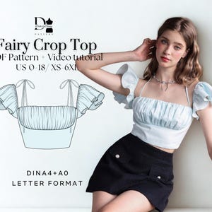 Könnte beinhalten: Ein hellblau-weißes Fairy Crop Top-Design mit quadratischem Ausschnitt und Rüschenärmeln. Das Bild enthält den Text "Fairy Crop Top PDF Pattern + Video tutorial US 0-18 / XS-6XL". Das Design wird von einem Model mit schwarzem Rock getragen.