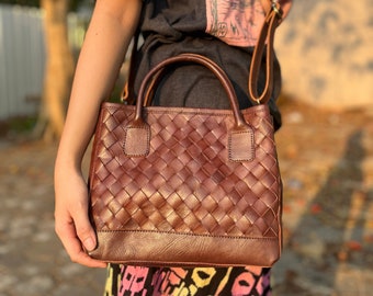 May include: A brown leather woven tote bag with a top handle and a shoulder strap. The bag has a woven pattern and a solid brown bottom.