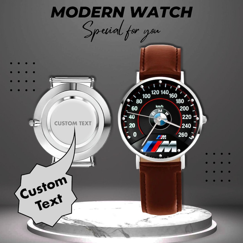 May include: Modern watch with a brown leather strap and a black speedometer-style face featuring the BMW logo. The watch face displays speed markings up to 260 km/h. A second watch with a silver case and space for custom text is also shown.