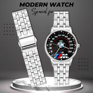 May include: A silver-toned wristwatch with a black dial featuring a speedometer design and the BMW logo. The watch has a matching silver band and the text "MODERN WATCH" is at the top.
