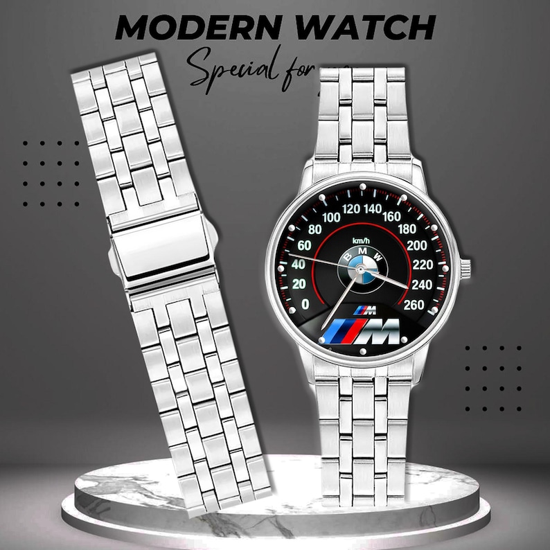 May include: A silver-toned wristwatch with a black dial featuring a speedometer design and the BMW logo. The watch has a matching silver band and the text "MODERN WATCH" is at the top.