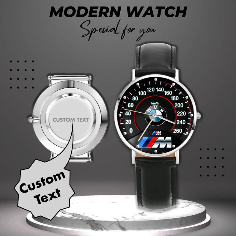 May include: A modern watch with a black face featuring a speedometer design, the BMW logo, and a black leather strap. The watch face displays numbers and markings in white. The watch is displayed next to a silver watch back with the text "CUSTOM TEXT".