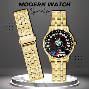 May include: A gold-toned wristwatch with a black speedometer-style face featuring the BMW logo and a matching gold band. The watch face displays numbers up to 260 km/h. The text "MODERN WATCH" and "Special for" are at the top.