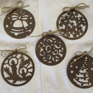 May include: Five rustic, brown, circular Christmas ornaments with cut-out designs. Each ornament is adorned with a twine bow for hanging. Designs include a bell, stars, swirling patterns, candles, and a Christmas tree.