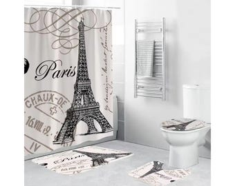 May include: A bathroom set with a shower curtain, toilet seat cover, and two bath mats. The shower curtain features a black and white illustration of the Eiffel Tower with the word "Paris" and a vintage stamp design. The toilet seat cover and bath mats have a similar design.