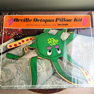 May include: A boxed "Orville Octopus Pillow Kit" with a green octopus design. The octopus has pink eyes, a yellow and red dotted tentacle, and the text "ANOTHER CREATIVE FUN-PROJECT from Sew Simple" on the box.