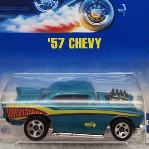 Puede incluir: Un coche de juguete Hot Wheels Chevrolet de 1957 azul y amarillo sobre un fondo azul con el texto '57 CHEVY' y el logotipo de Hot Wheels. El coche tiene un interior negro y ruedas negras.