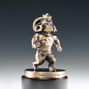 Puede incluir: Una estatua de bronce de una mascota de carnero con un sombrero de marinero y una camiseta con el texto "UNIVERSITY OF NORTH" en la base.