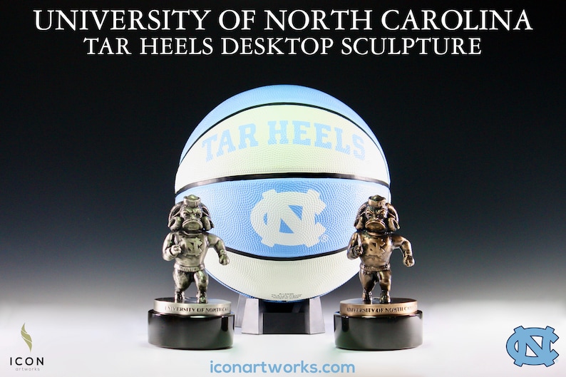 Puede incluir: Una escultura de escritorio de los Tar Heels de la Universidad de Carolina del Norte en plata y bronce con un bal&oacute;n de baloncesto y dos mascotas. El bal&oacute;n de baloncesto es azul y blanco con las palabras "Tar Heels" impresas en &eacute;l. Las mascotas est&aacute;n de pie sobre bases negras con las palabras "University of North Carolina" impresas en ellas.