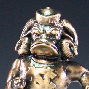 Puede incluir: Una figurita de bronce de una mascota que lleva un gorro de marinero con las letras "UNC" en &eacute;l. La mascota tiene una cara grande y expresiva y lleva una camisa con un gran logotipo de "UNC".