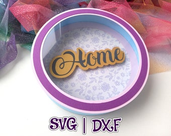May include: A round, layered paper craft with a purple, blue, and white frame. The center features a floral pattern and the word "Home" in a gold and black font.