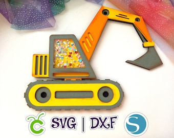 May include: Yellow and orange wooden toy excavator with a clear plastic window filled with colorful beads. The excavator has a black scoop and a black track. The text "SVG | DXF" is printed below the excavator.