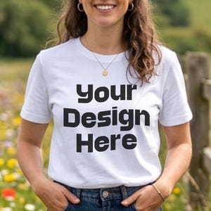 May include: A white short-sleeved t-shirt featuring the black text Your Design Here printed on the front. The garment has a crew neckline and is worn with blue denim jeans that have a button and zipper closure at the center front waist.
