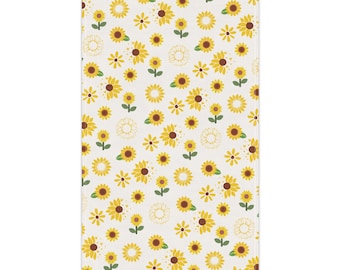 May include: A white kitchen towel with a repeating pattern of yellow sunflowers. The sunflowers have brown centers and green stems.