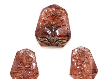 May include: Three carved gemstone pendants with a flower design. The gemstones are a deep reddish-brown color and have a translucent appearance.