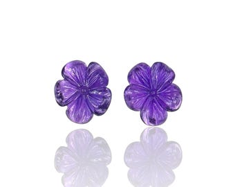 May include: A pair of deep purple amethyst gemstones carved into the shape of five-petaled flowers. Each gemstone features intricate petal detailing and a smooth, polished surface, reflecting light to showcase the vibrant violet color.