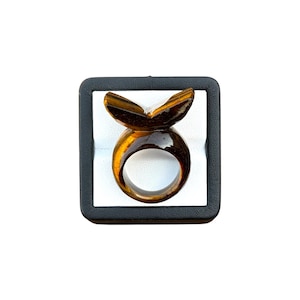 Op de afbeelding: Een bruin en goudkleurige tijgeroogring, gepresenteerd in een zwart-witte doos. De ring heeft een vlindervormige bovenkant en een afgeronde band. Het ontwerp is uniek.