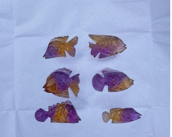 May include: Six carved gemstone fish figurines arranged in two columns. Each piece features a gradient of translucent purple and golden yellow hues, with detailed etched scales, fins, and eye markings visible on the polished surfaces of the stones.