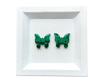 May include: Two butterfly-shaped buttons crafted from green malachite stone. Each button features distinct dark green banding patterns and two small holes positioned in the center for attachment, showcasing the natural mineral texture.