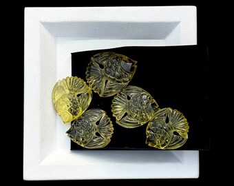 May include: Five translucent, pale yellow, fish-shaped carvings made of a clear material. Each piece features detailed etched lines representing scales and fins, arranged in a cluster on a black rectangular surface set within a white square frame.