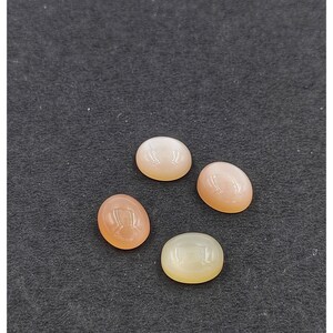 May include: Four oval-shaped moonstone cabochons in various shades of white and peach.