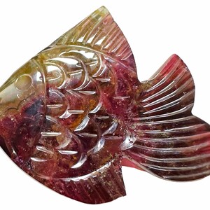 May include: A carved gemstone fish sculpture. The fish is a mix of colors, including yellow, red, and purple. The sculpture has detailed carvings of scales and fins. The fish is a decorative item.