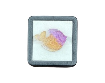 May include: A carved gemstone fish figurine featuring a gradient color transition from a translucent purple head to a golden yellow tail and body, displayed inside a square black jewelry box with a white velvet interior lining.