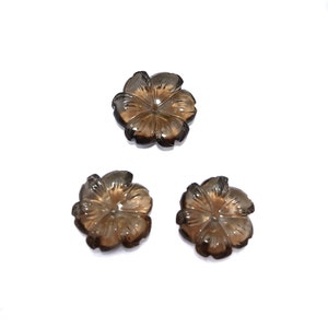 May include: Three carved smoky quartz flower cabochons. Each flower has six petals and a center hole. The flowers are a light brown color.