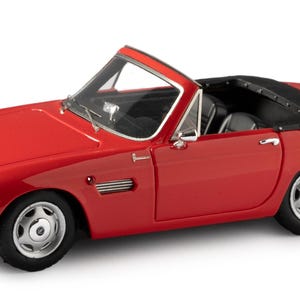 May include: A red convertible sports car model with a black fabric top. The car has a chrome bumper and silver wheels.